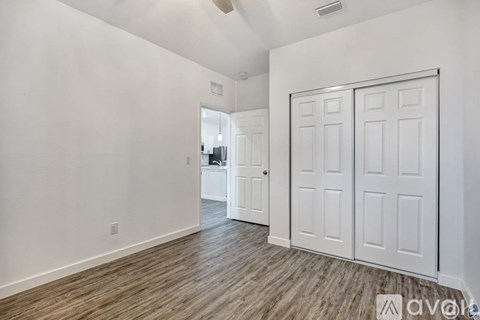 A room with white walls and a wooden floor with a white door on the right.
