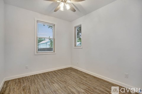A room with a ceiling fan and two windows.