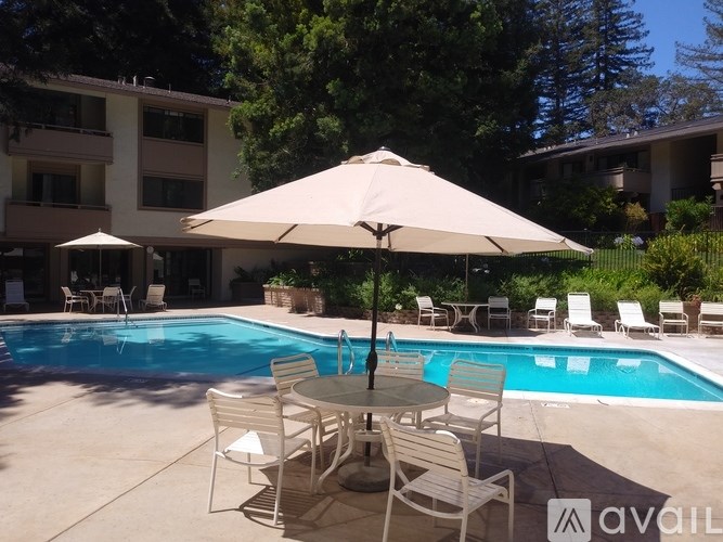 A pool with chairs and an umbrella in the foreground with apartment buildings in the background.
