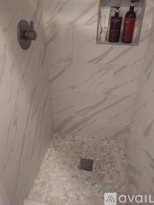 A white marble tiled shower with a silver faucet and a shelf with two bottles of soap.