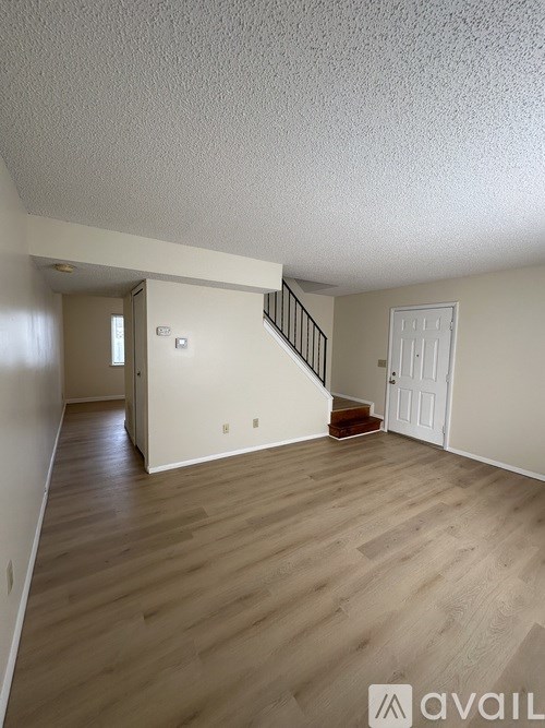 A spacious room with wooden floors and a staircase leading to another room.