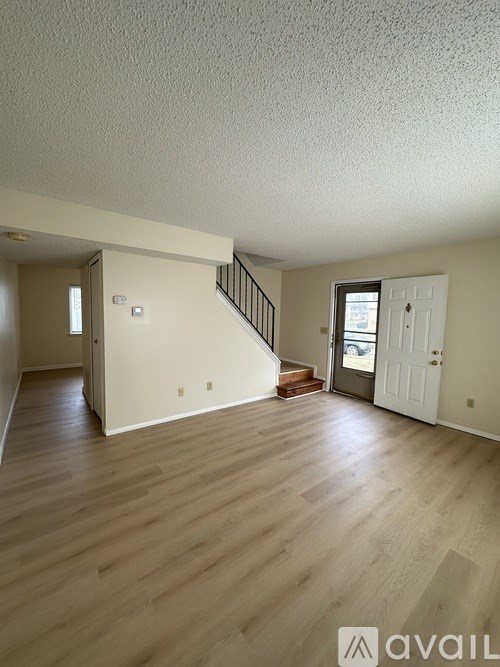 A spacious room with wooden floors and a staircase leading to another room.