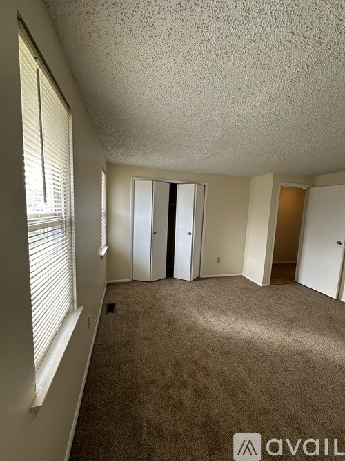 A carpeted room with a window and a door leading to another room.