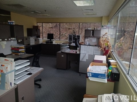 A cluttered office space with a desk, chairs, and filing cabinets.