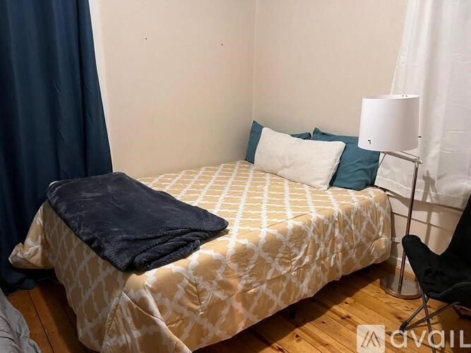 A bed with a white and tan patterned comforter and a black blanket on top.