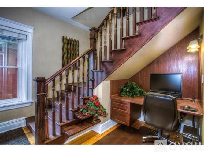 A home office with a wooden desk and a chair is located under a staircase.