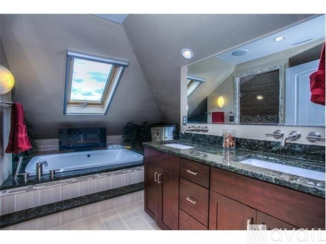 A bathroom with a skylight, a bathtub, a sink, and a television.
