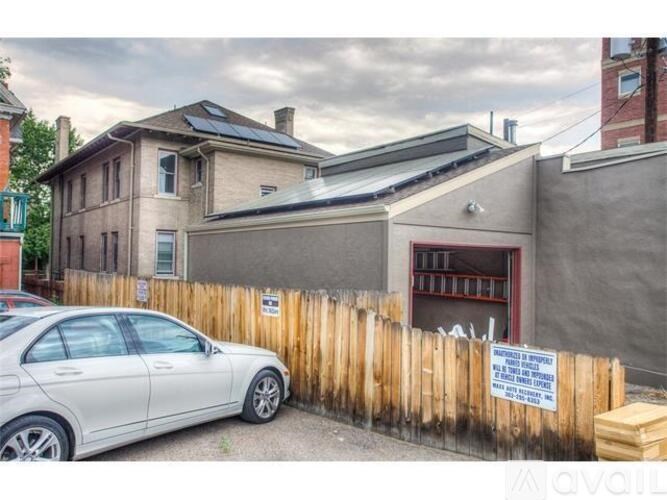 A car is parked in front of a house with a sign on the fence.