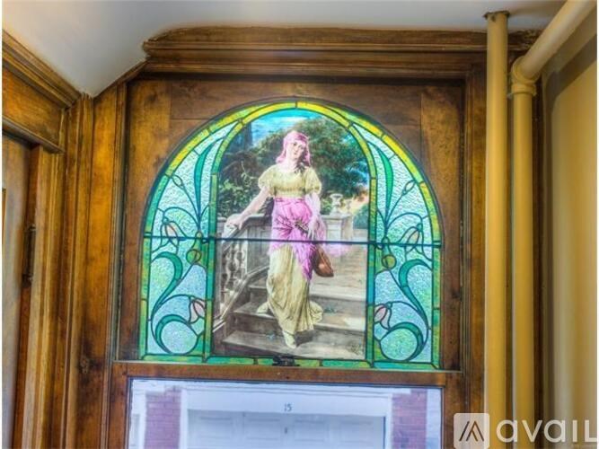 A stained glass window depicting a woman in a pink dress is framed in a wooden archway.