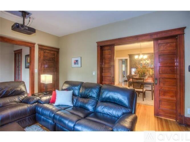 A black leather couch in a living room with a television on the wall.
