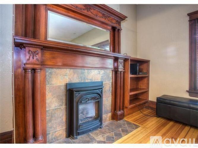 A wood fireplace with a black grate in a room with wooden floors.