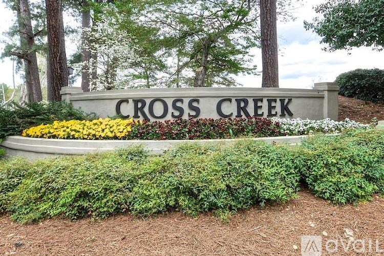 A sign that says "Cross Creek" is surrounded by bushes and flowers.