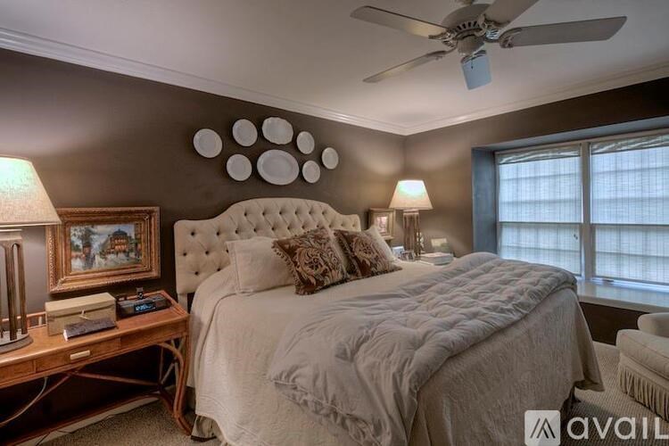 A bedroom with a large bed, a ceiling fan, and a painting on the wall.