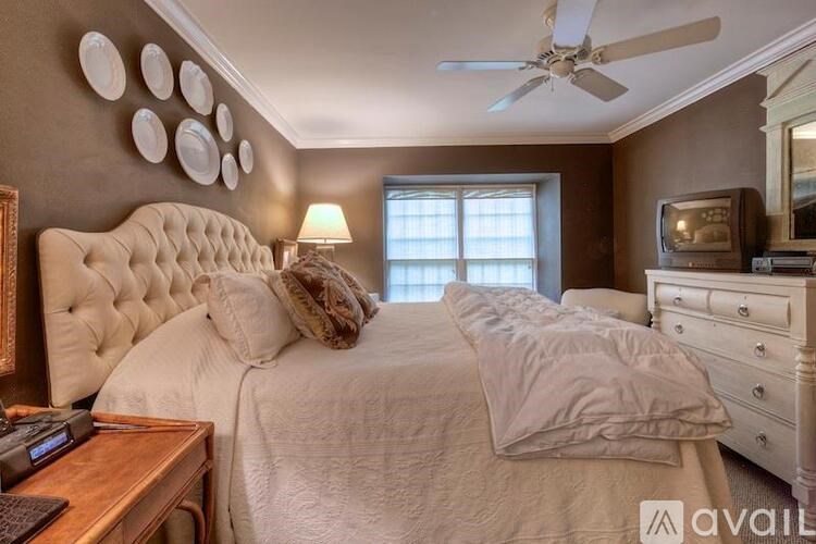 A bedroom with a large bed, a ceiling fan, and a dresser with a television on top.