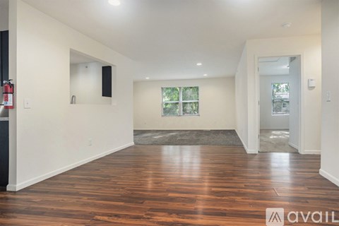 A spacious room with wooden floors and a window with a view of trees.