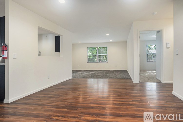 A spacious room with wooden floors and a window with a view of trees.