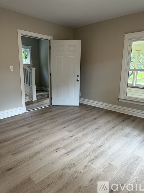 A room with a white door and a window with a view of trees.