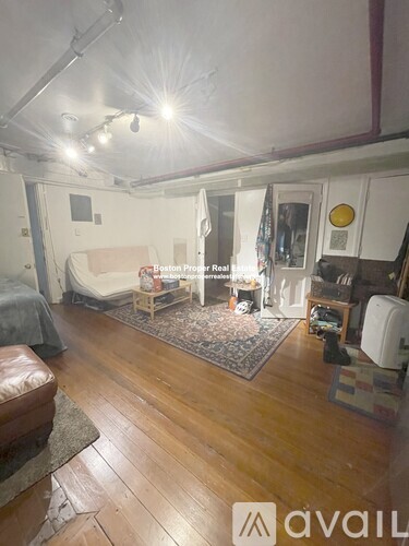 A living room with a couch, a rug, and a bed in the background.