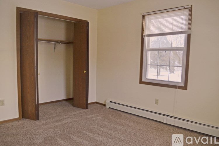 A room with a carpeted floor, a window with blinds, and a door that is open.