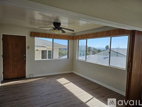 A room with a ceiling fan and large windows overlooking a street.