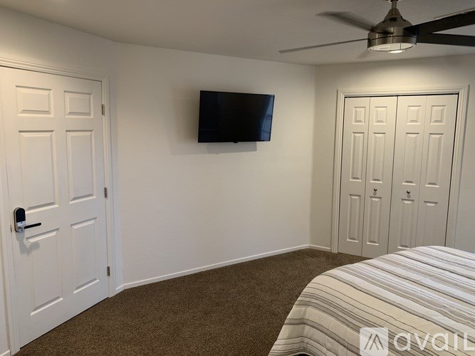 A bedroom with a bed, a ceiling fan, and a flat-screen TV mounted on the wall.
