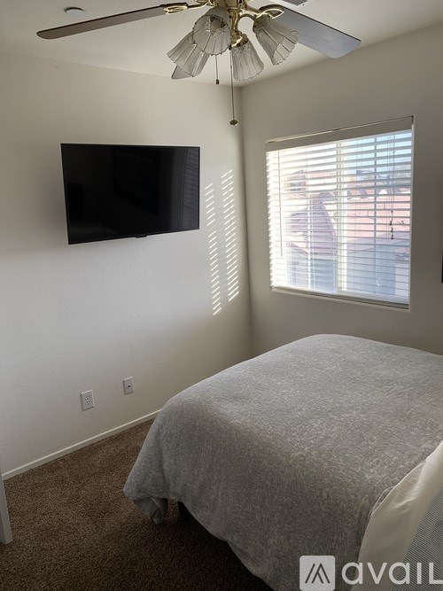 A bedroom with a bed, ceiling fan, and a flat screen TV mounted on the wall.