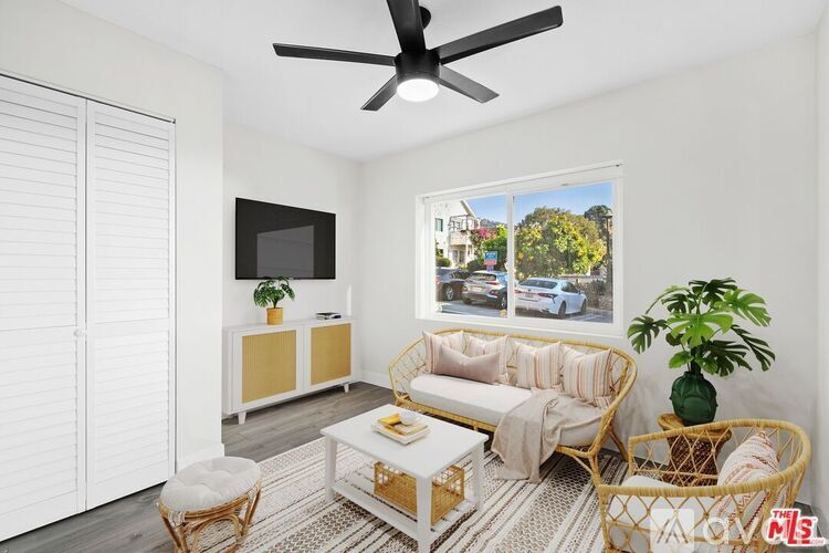 A living room with a white sofa, a white coffee table, a white ceiling fan, and a white wall with a window.