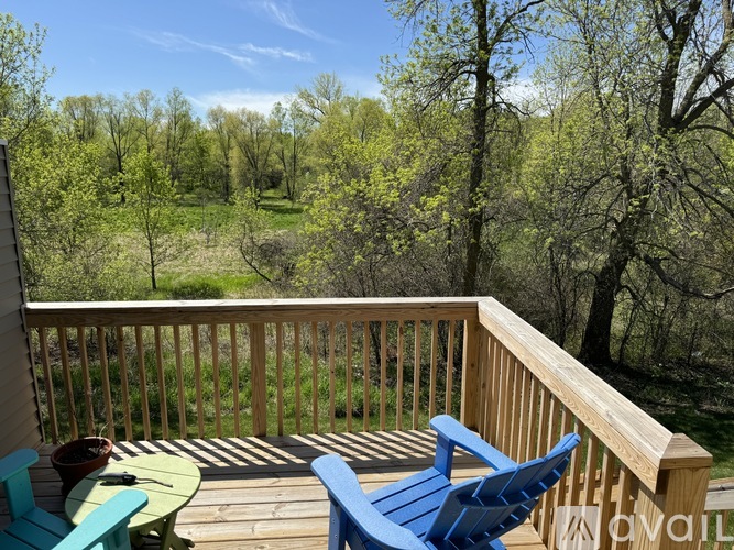 A wooden deck with blue chairs and a table overlooks a green landscape.