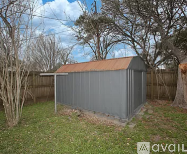 A grey shed with a brown roof is situated in a grassy area.