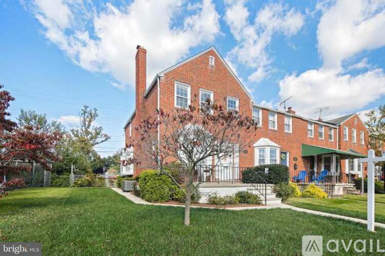 A large red brick house with a white fence and a tree in front.