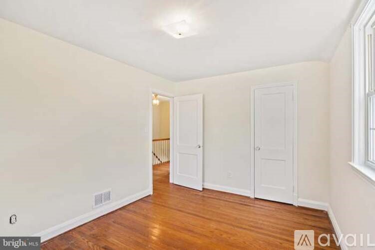 A room with wooden floors and white walls, with two doors and a window.