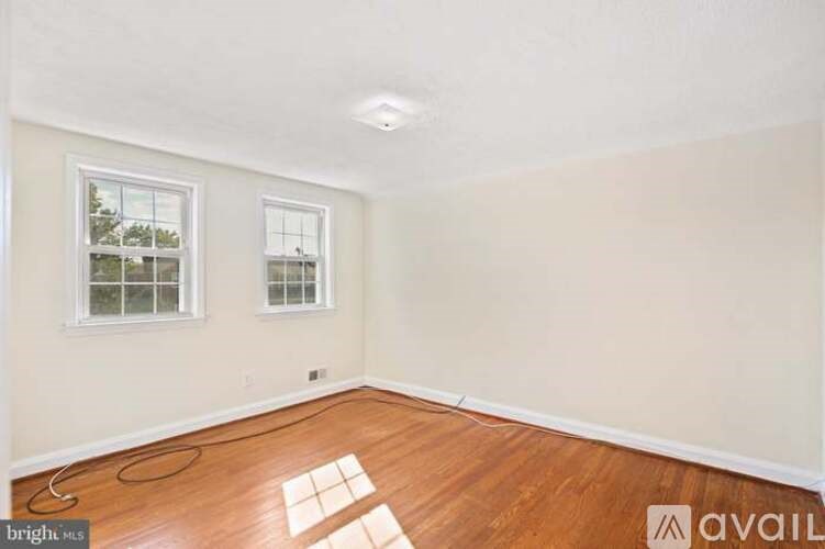 A room with wooden flooring and two windows is available for rent.