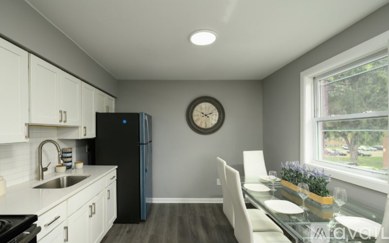 A modern kitchen with a black refrigerator, white cabinets, and a glass dining table.