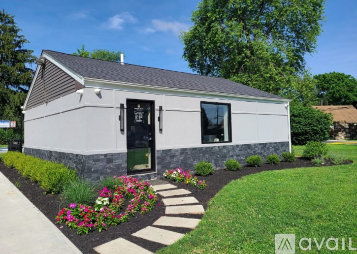A small house with a black door and windows is surrounded by a garden with flowers.