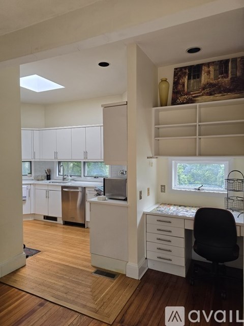 A kitchen with white cabinets and a window with a black chair in front of it.