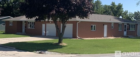 A red brick house with a white garage door and a tree in front.