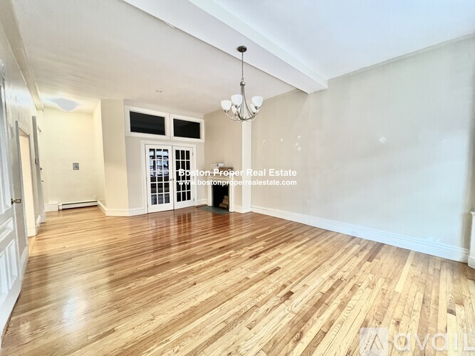 A spacious room with wooden flooring and a chandelier.