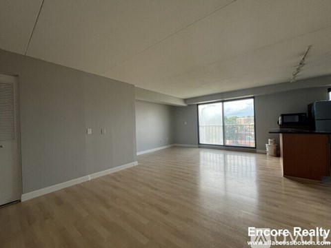 A spacious room with wooden flooring and a sliding glass door leading to a balcony.
