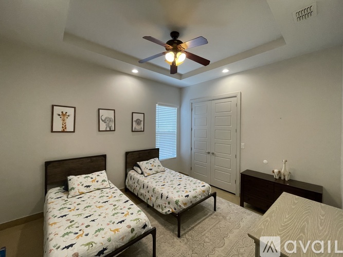A bedroom with two beds, a ceiling fan, and framed pictures on the wall.