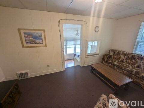 A living room with a couch, a painting on the wall, and a window.