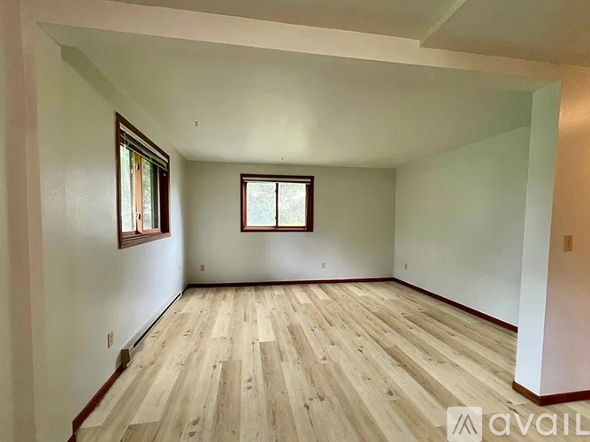 A spacious room with wooden flooring and two windows.