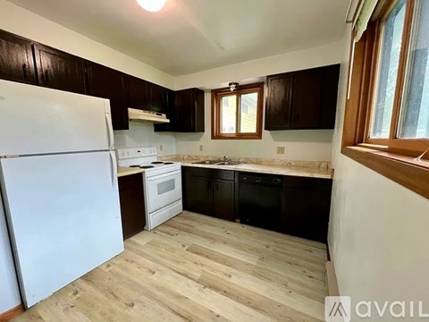 A kitchen with a white fridge, black cabinets, and wooden floors.