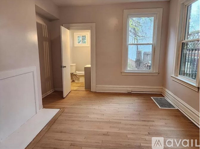 A room with wooden flooring and a window showing a view of a fence and trees.