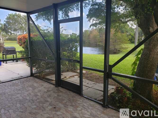 A glass door with a metal frame leads to a patio with a view of a pond and trees.