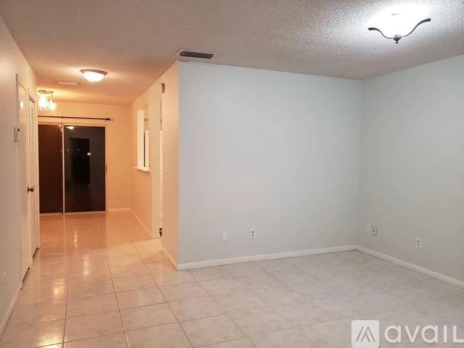 A spacious room with tiled flooring and white walls, with a door on the left and a light fixture on the ceiling.