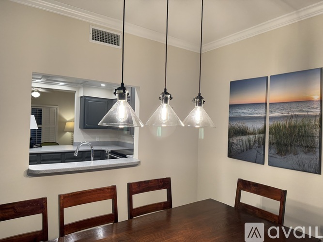 A dining room with a wooden table and chairs, a kitchen area with a sink and a mirror, and a painting of a beach scene on the wall.