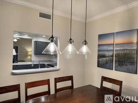 A dining room with a wooden table and chairs, a kitchen area with a sink and a mirror, and a painting of a beach scene on the wall.