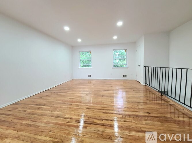 A spacious room with wooden flooring and two windows.