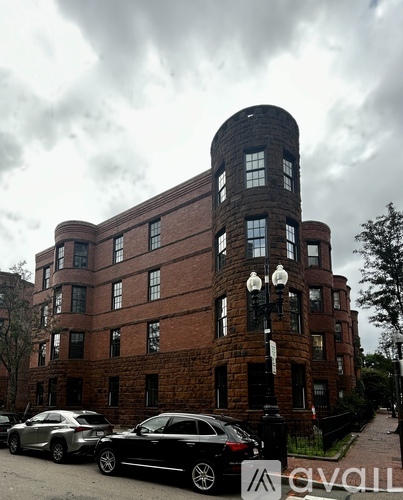 A tall red brick building with a round tower and a black car parked in front.