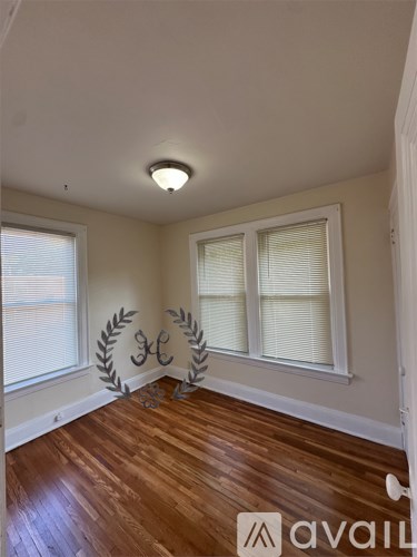 A room with wooden floors and two windows with white blinds.